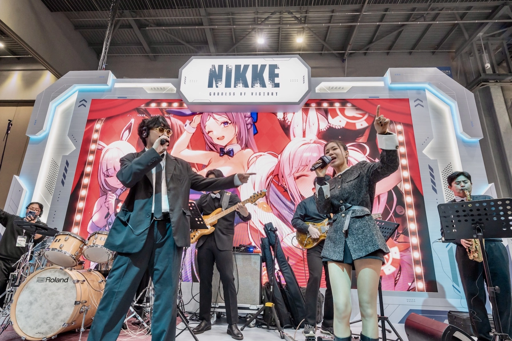 Male and female vocalists performing with a live band on the NIKKE stage