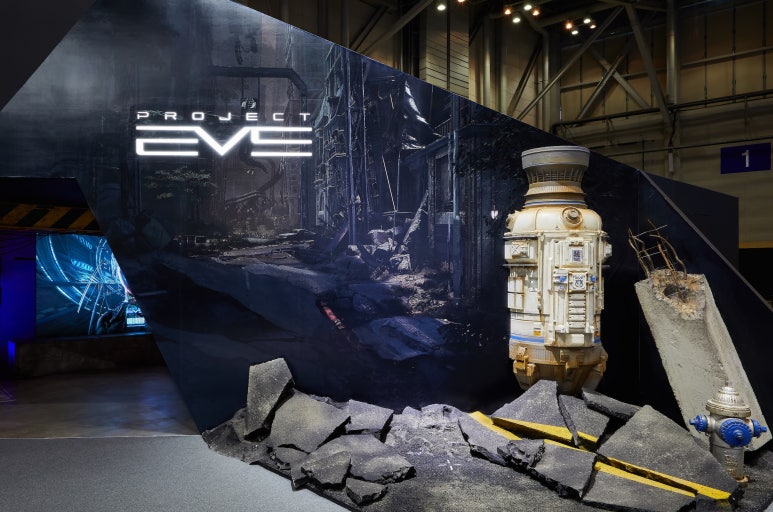 Large-scale game exhibition hero installation featuring Project EVE: a sci-fi escape pod embedded in a fractured wall, surrounded by broken concrete debris and a futuristic urban backdrop inside a convention hall.