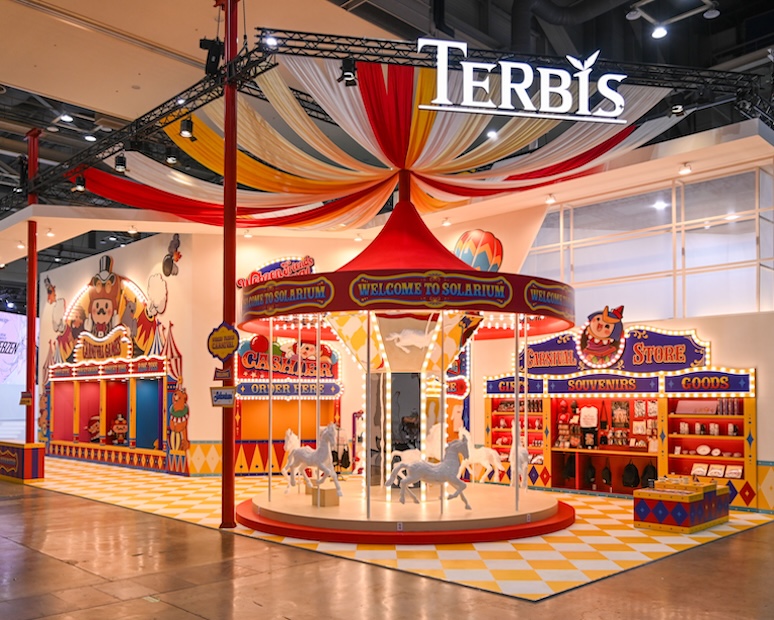 WEBZEN Friends Carnival booth at G-STAR 2025, centered around a working carousel beneath the Terbis signage, flanked by carnival game stalls and a souvenir store.