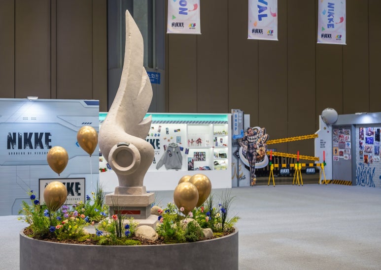 NIKKE booth with a central sculptural installation, flowers, and gold balloons.